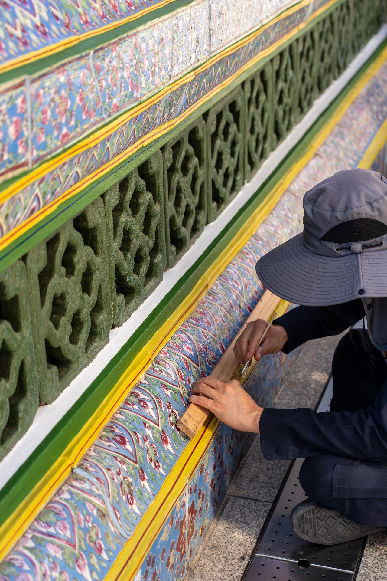 A person in a blue hat is working on a colorful, ornate wall with intricate designs.