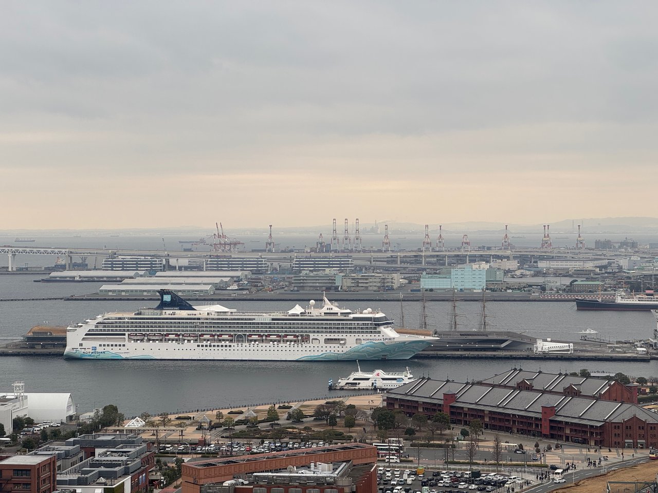 A bustling harbor scene features a large white cruise ship docked in the harbor, surrounded by smaller boats and a cityscape in the background.