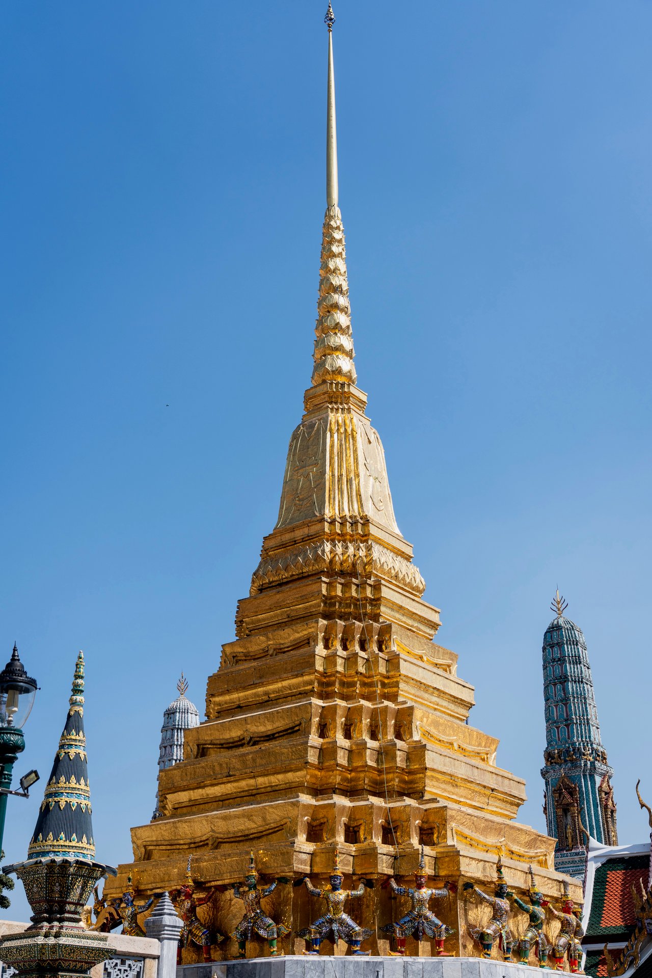 The image captures the majestic Wat Phra Kaew temple in Bangkok, Thailand, with its golden spire reaching towards the clear blue sky.