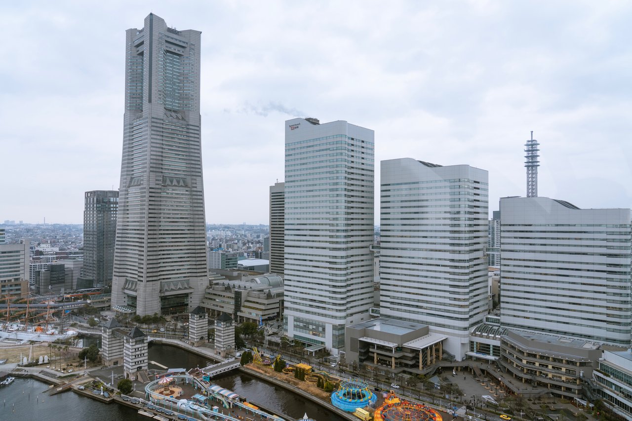 An aerial view of a cityscape with modern skyscrapers, a river, and a bridge, showcasing a blend of urban development and natural elements.