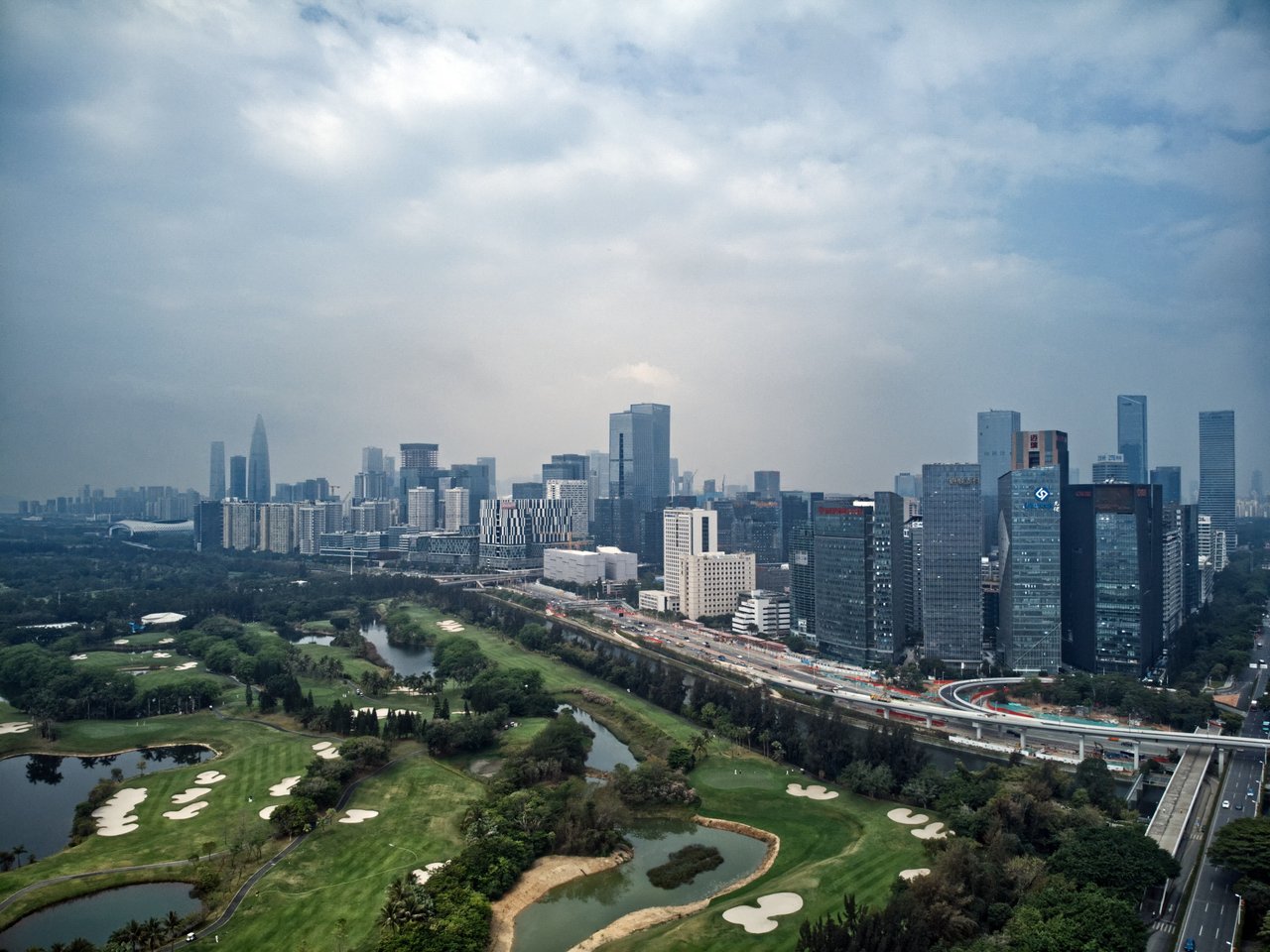 A bustling cityscape with towering skyscrapers, a park with lush greenery, and a highway running through it.