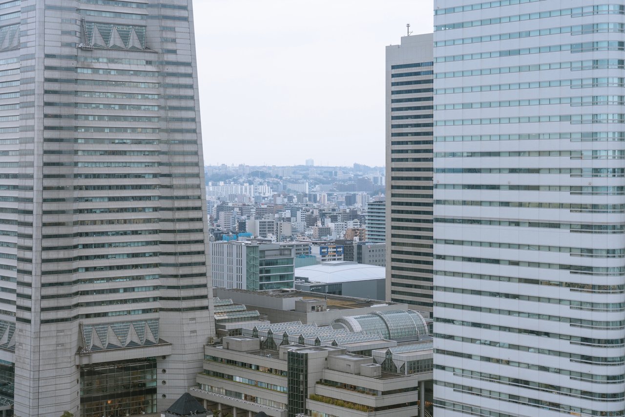 A cityscape with skyscrapers, a large building, and a few smaller ones, surrounded by a hazy sky.