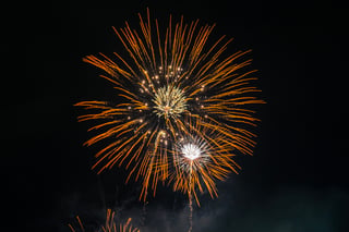 A fireworks display in the night sky, with bright orange and yellow fireworks, creating a dazzling spectacle against the black sky.