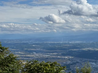 A serene mountainous landscape with a vast valley in the background, surrounded by lush greenery and a few scattered trees. The sky is filled with fluffy white clouds, creating a picturesque backdrop. A few birds are seen flying in the sky, adding life to the scene.