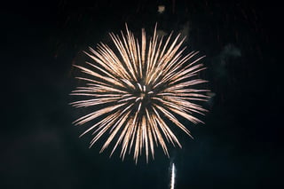 A large, radiant firework explosion illuminates the night sky, with a single bright light emanating from the center. The explosion is surrounded by a dark sky, creating a dramatic contrast.
