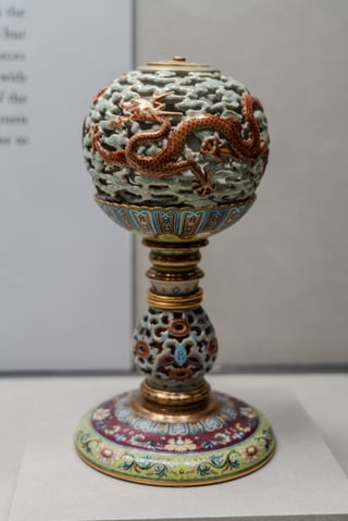 A decorative cup with a dragon design on a gold base, placed on a white surface.