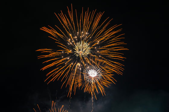 A fireworks display in the night sky, with bright orange and yellow fireworks, creating a dazzling spectacle against the black sky.