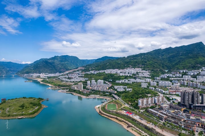 An aerial view of a city nestled between mountains, with a large body of water in the foreground and a cityscape in the background.