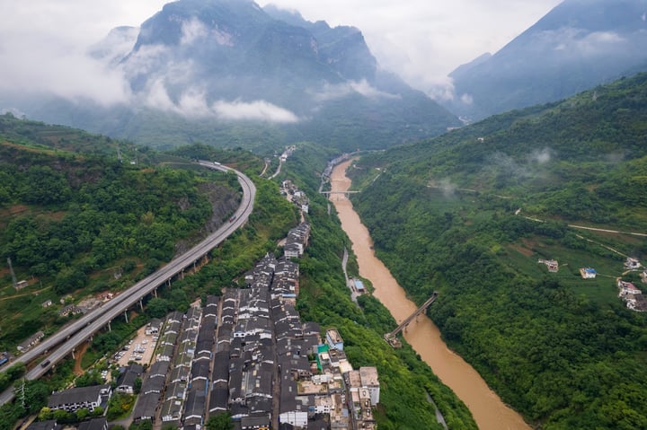 An aerial view of a mountainous landscape with a winding river, a highway, and a mountain range in the background.