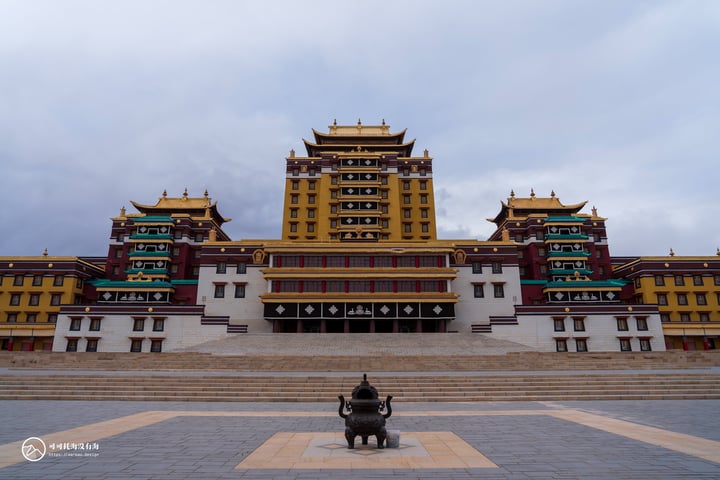 A grand, multi-level Chinese temple with a yellow facade and red accents stands in a courtyard, surrounded by a stone statue of a lion. The temple is flanked by a set of stone steps, and the sky is filled with clouds.