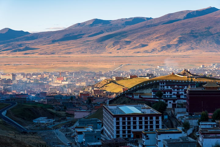 A panoramic view of Potala, a city in Tibet, with a mountain range in the background and a clear blue sky above.