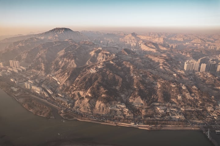 An aerial view of a mountainous landscape with a river, a city, and a bridge, showcasing a harmonious blend of nature and urban development.