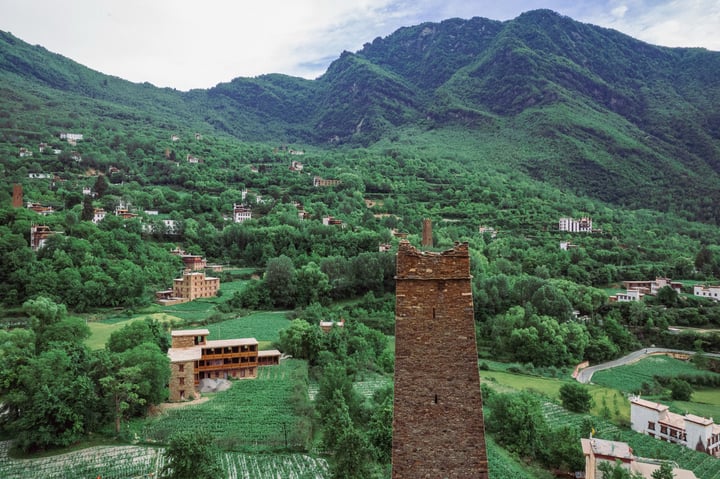 A serene mountainous landscape with lush greenery, a quaint village, and a tall brick tower in the foreground.