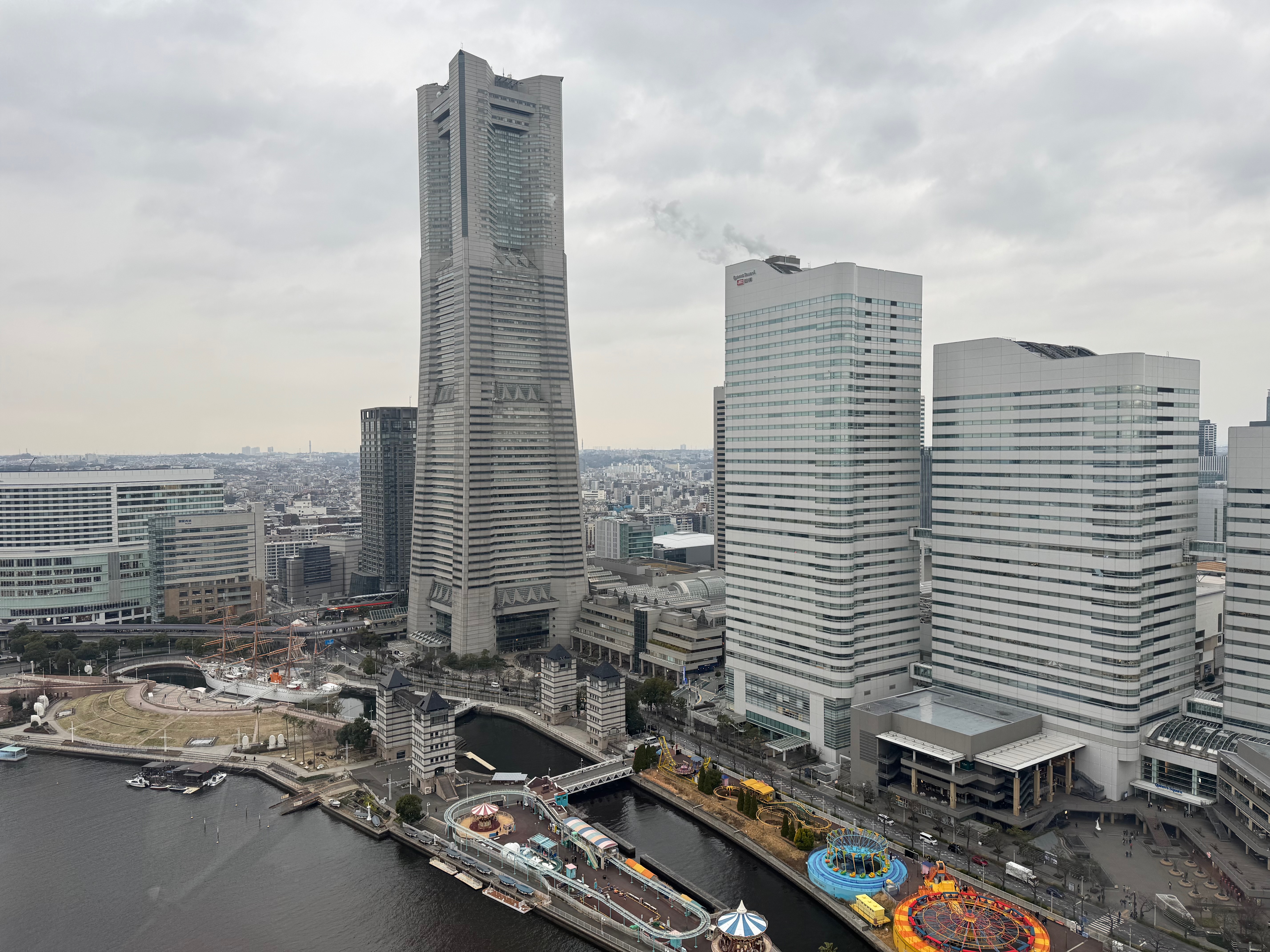 A panoramic view of Tokyo's skyline, featuring a tall skyscraper, a modern building, and a bridge over a river, with a cloudy sky above.