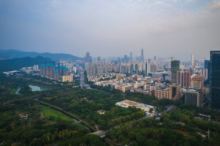 An aerial view of a bustling city with tall buildings, a river, and mountains in the background, showcasing a harmonious blend of urban development and natural beauty.