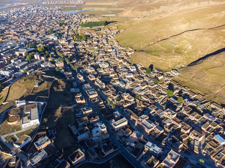 An aerial view of a town nestled in a valley, surrounded by hills and fields, with buildings of varying sizes and colors, creating a vibrant and diverse landscape.