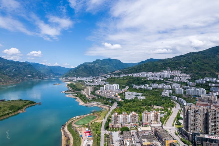 An aerial view of a city nestled between mountains, with a large body of water in the foreground and a cityscape in the background.