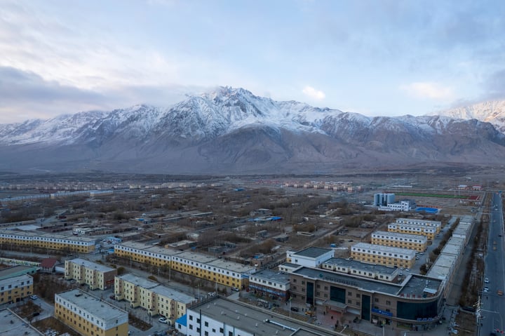 A panoramic view of a snow-capped mountain range, with a cityscape in the foreground, surrounded by trees and buildings.