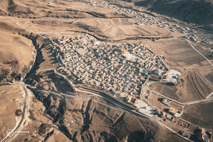 An aerial view of a town nestled in a valley, surrounded by rolling hills and a vast expanse of brown dirt, with roads and buildings scattered throughout.