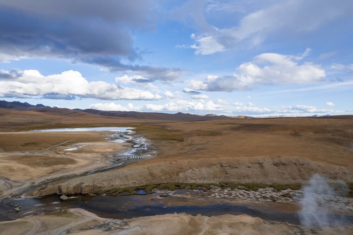 A vast, barren landscape with a river flowing through it, surrounded by mountains and a cloudy sky.