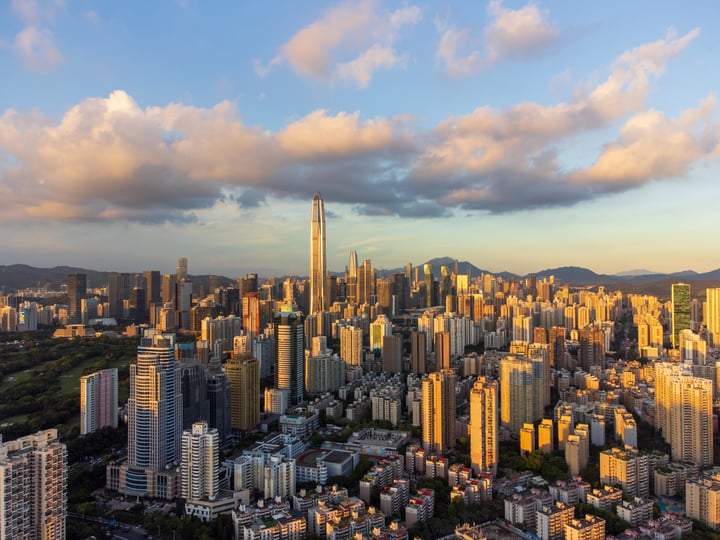 An aerial view of a bustling city with tall buildings, a prominent skyscraper, and a mountain range in the background.