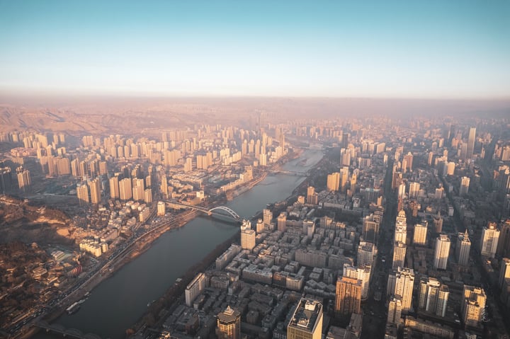 An aerial view of a bustling city with tall buildings, a river, and bridges, all set against a clear blue sky.
