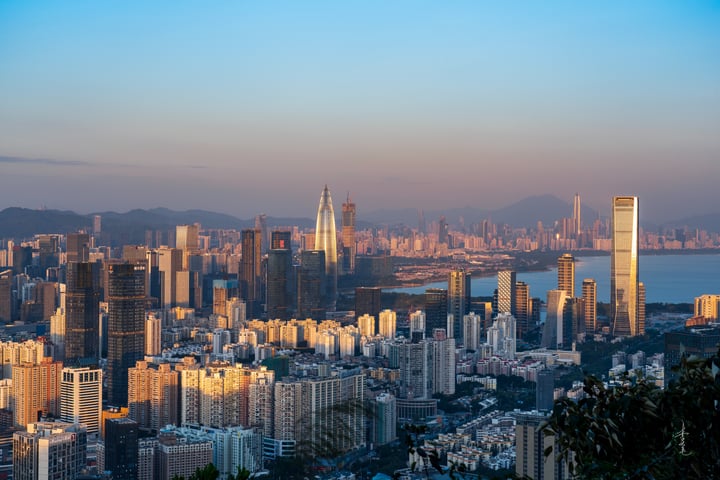 A panoramic view of Hong Kong's skyline, featuring a mix of modern and traditional buildings, with the iconic World Trade Center and the iconic One% building standing out. The city is nestled between mountains, and the sky is a mix of blue and orange hues.