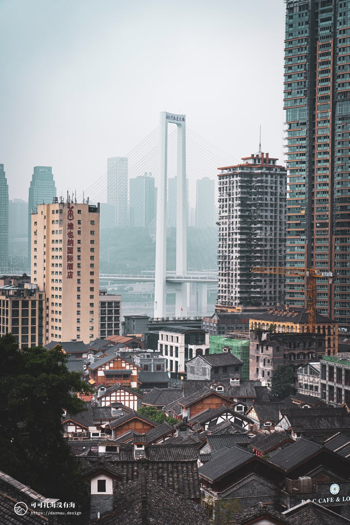A cityscape with tall buildings, a bridge, and a few cranes, with a cloudy sky.