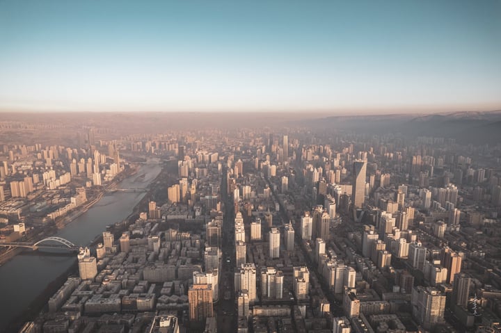 An aerial view of a bustling city with tall buildings, a river, and bridges, all set against a clear blue sky.