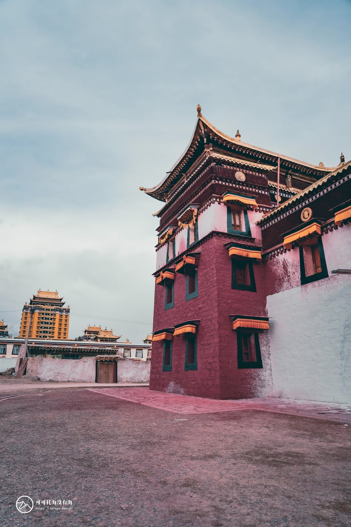 A traditional Chinese building with a red and white facade, gold accents, and a green roof stands in a courtyard, surrounded by other buildings and a cloudy sky.