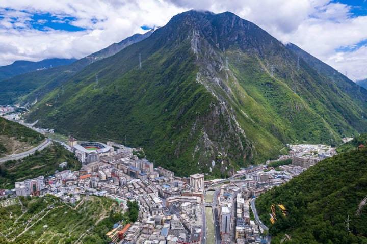 A panoramic view of a mountain town nestled amidst lush greenery, with a winding road winding through the town and a mountain range in the background.