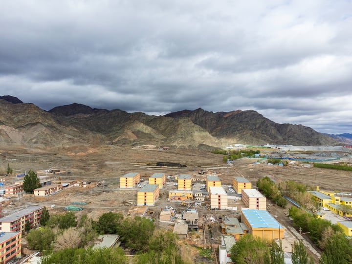 A mountainous area with a cityscape in the foreground, with a cloudy sky overhead.
