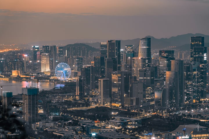 A nighttime cityscape features illuminated skyscrapers, a large Ferris wheel, and mountains in the background.