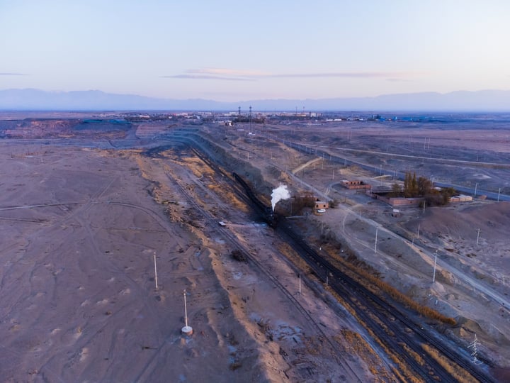 An aerial view of a large construction site with a dirt road, a train track, and a large tunnel.