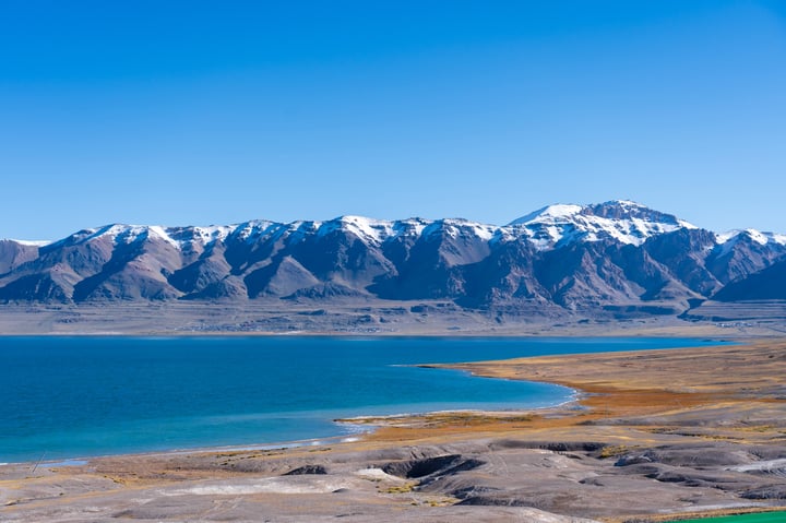 A breathtaking view of a mountain range with snow-capped peaks, a deep blue lake, and a vast expanse of sky.