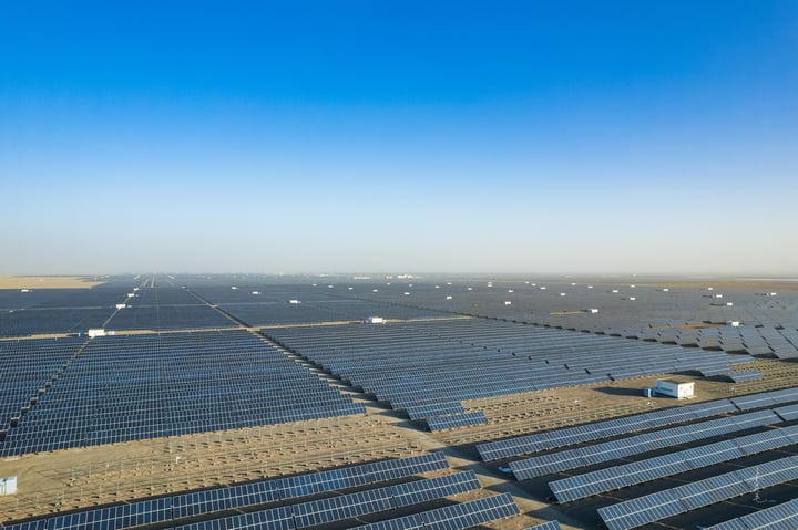 An aerial view of a large solar farm with rows of solar panels in a desert-like environment.