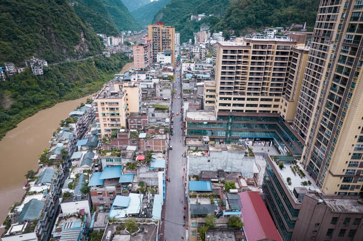An aerial view of a city with a river, tall buildings, and green mountains, showcasing a harmonious blend of urban development and natural beauty.