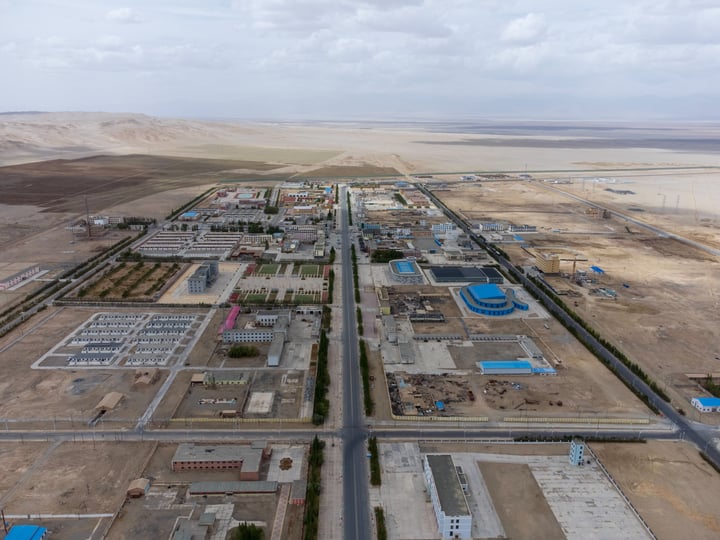 An aerial view of a large industrial area with a grid of roads, buildings, and a large water body in the background.