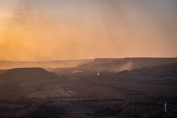 A sunset over a desert landscape, with a warm orange glow, a dusty road, and a small figure on a hill.