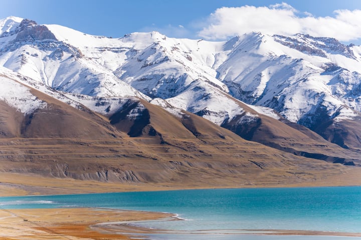 A serene mountain landscape with snow-capped peaks and a tranquil lake in the foreground.