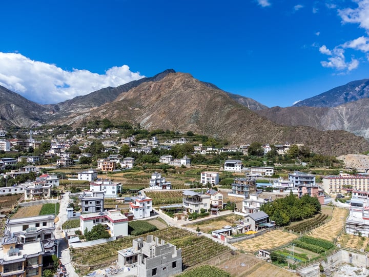 A picturesque mountain town with white buildings, green fields, and a clear blue sky.