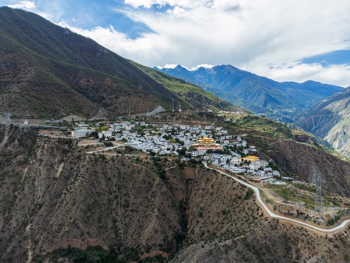 A picturesque mountain town nestled amidst lush greenery, surrounded by towering mountains and a winding road.
