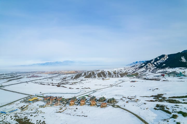 A snowy mountain landscape with a clear blue sky, a winding road, and a small village in the valley.
