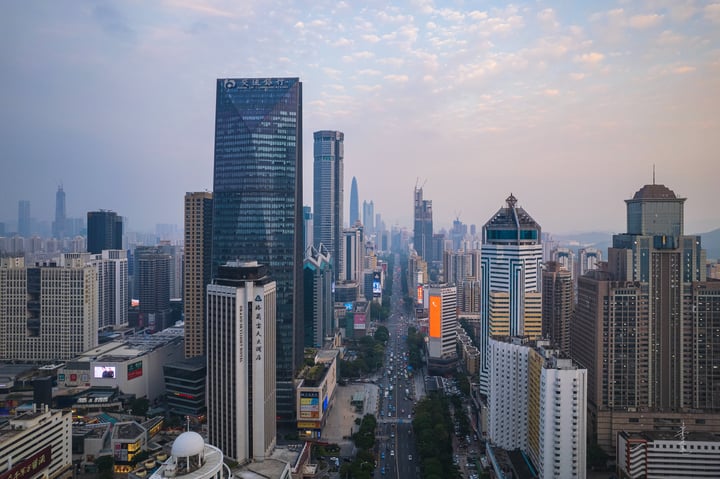 A panoramic view of a bustling cityscape with tall buildings, a busy road, and a hazy sky.