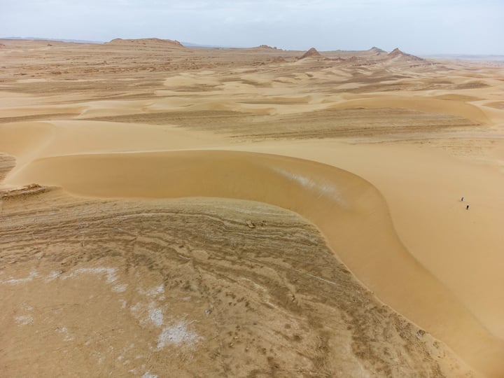 A vast desert landscape with sand dunes, a cloudy sky, and a few small rocks scattered across the landscape.