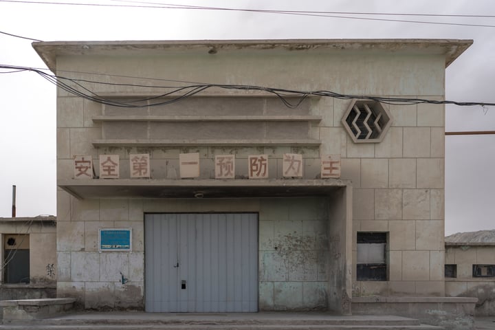 A large, dilapidated building with a blue door and a window on the second floor, surrounded by power lines and a telephone pole.