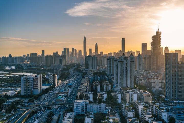 A city skyline at sunset, with tall buildings and a highway, illuminated by the setting sun.