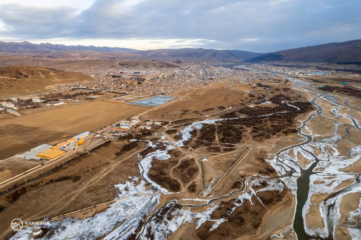 An aerial view of a mountainous landscape with a river, a city, and a bridge, showcasing a blend of nature and urban development.