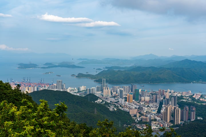 A panoramic view of Shenzhen's cityscape, with a cityscape of tall buildings and a large body of water in the background, surrounded by mountains and greenery.