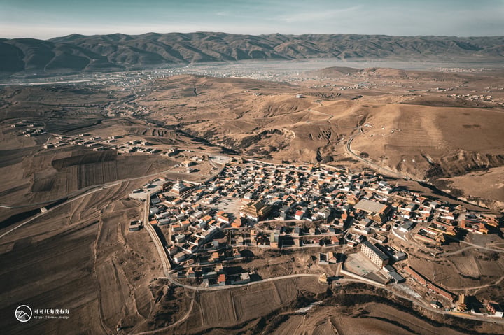 An aerial view of a small town nestled in a valley, surrounded by mountains and fields, with a clear blue sky above.